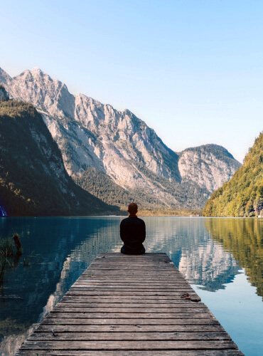 Une personne assise devant un lac miroir illustrant l'introspection analytique en psycho-généalogie, onirothérapie, thérapie par l'art et le traitement des traumas avec des outils de PNL