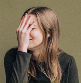 jeune femme en T-shirt ou pull vert, protégeant son visage de sa main, avec sourire, illustrant la clientèle ou patientèle en thérapie et coaching